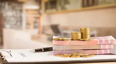 A stack of coins and banknotes on a paper and pen