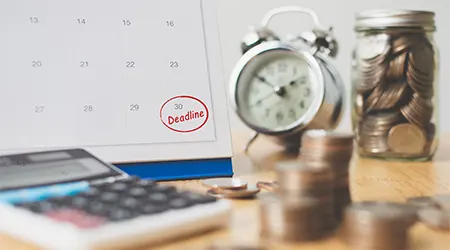 A calculator against stack of coins, a calendar and an alarm